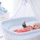 Funny baby in white crib with canopy. Nursery interior and bedding for kids. Laughing little boy playing in moses basket. Bedroom with bassinet for young children. Happy child in colorful pajamas.